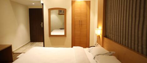 Una habitación de hotel con una cama grande, un armario de madera, un espejo y una cortina a rayas.
