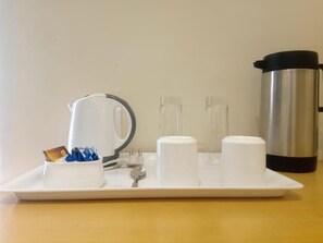 Una bandeja con una tetera eléctrica blanca, una taza blanca y tres recipientes de azúcar blancos sobre una mesa de madera.