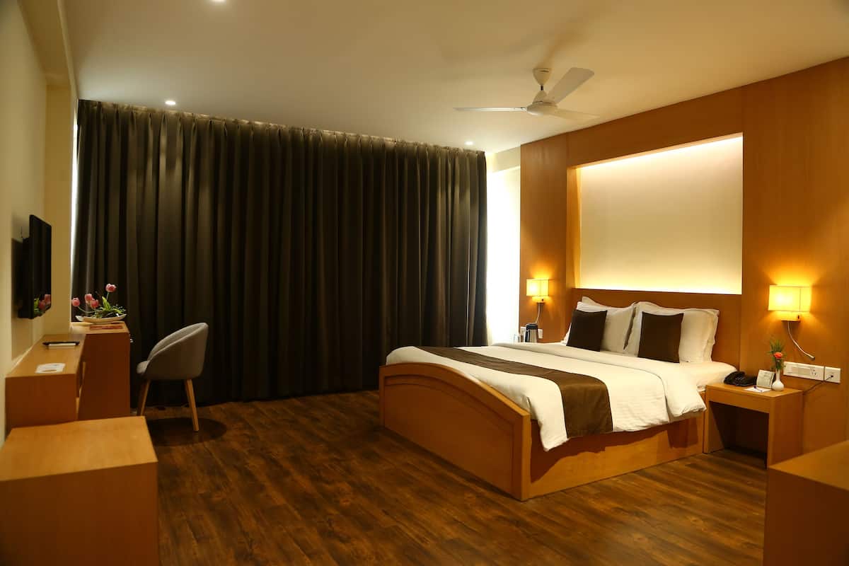 Habitación de hotel con cama de madera, escritorio, silla y ventana grande con cortinas.