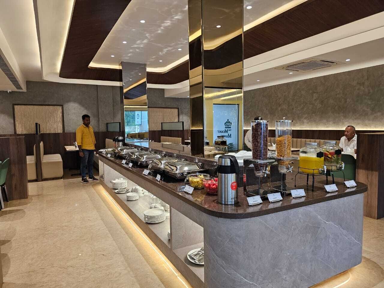 Un espace moderne pour le petit-déjeuner à l’hôtel, avec un buffet proposant divers plats présentés dans des récipients et une machine à café.