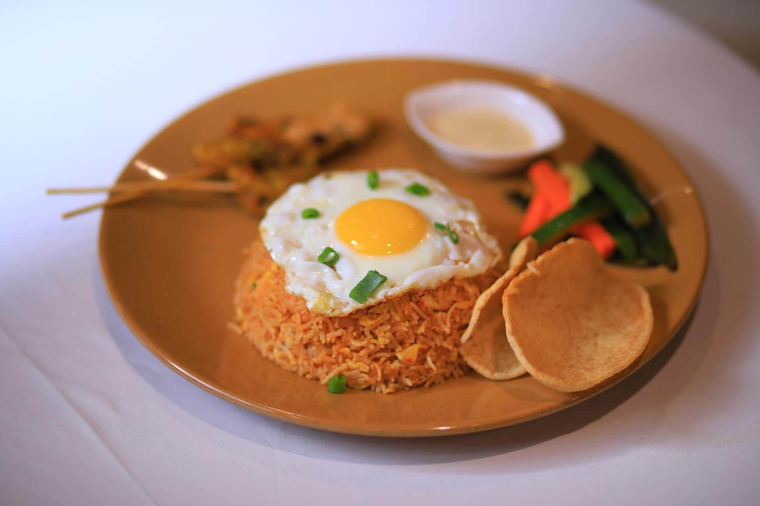 A plate of fried rice with a fried egg on top, accompanied by a small bowl of sauce and some vegetables.