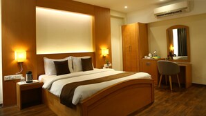 A hotel room with a bed, bedside tables, a desk, a chair, a ceiling fan, and an air conditioning unit. - Hotel Mount Manor (Chennai)