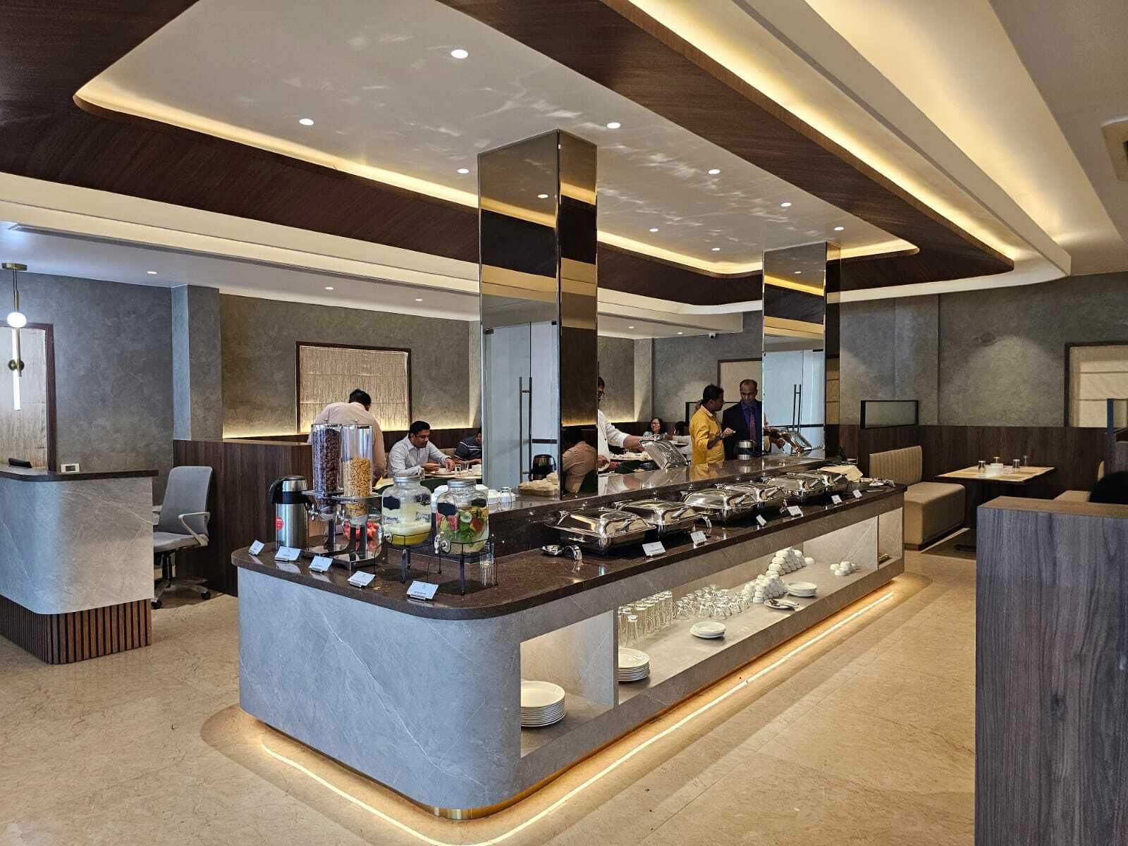 A modern hotel lobby with a self-service buffet, seating areas, and a reception desk.