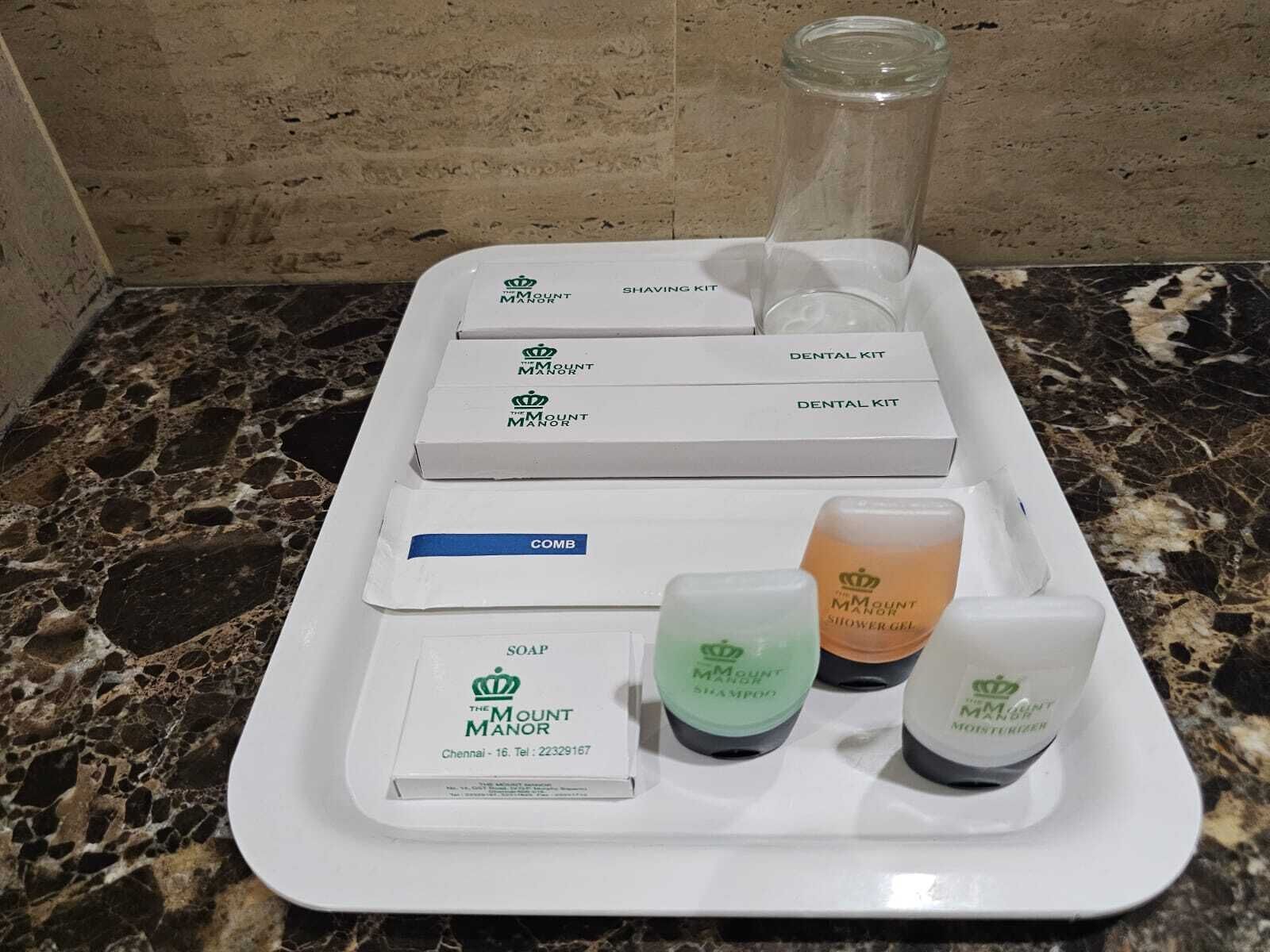 Uma toucador de banheiro com uma bandeja branca contendo kit de barbear, pente, sabonete, shampoo e gel de banho.