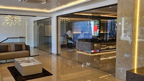 A modern lobby with a glass partition, a reception desk, and a sofa. - Hotel Mount Manor (Chennai)
