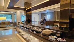A modern hotel lobby with a buffet area featuring various food items and a seating area with a sofa and chairs. - Hotel Mount Manor (Chennai)