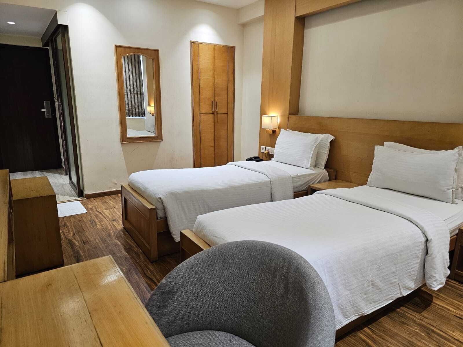A hotel room with two beds, a wooden wardrobe, a desk, and a chair.