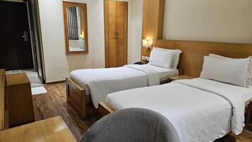 A hotel room with two beds, a wooden wardrobe, a desk, and a chair.