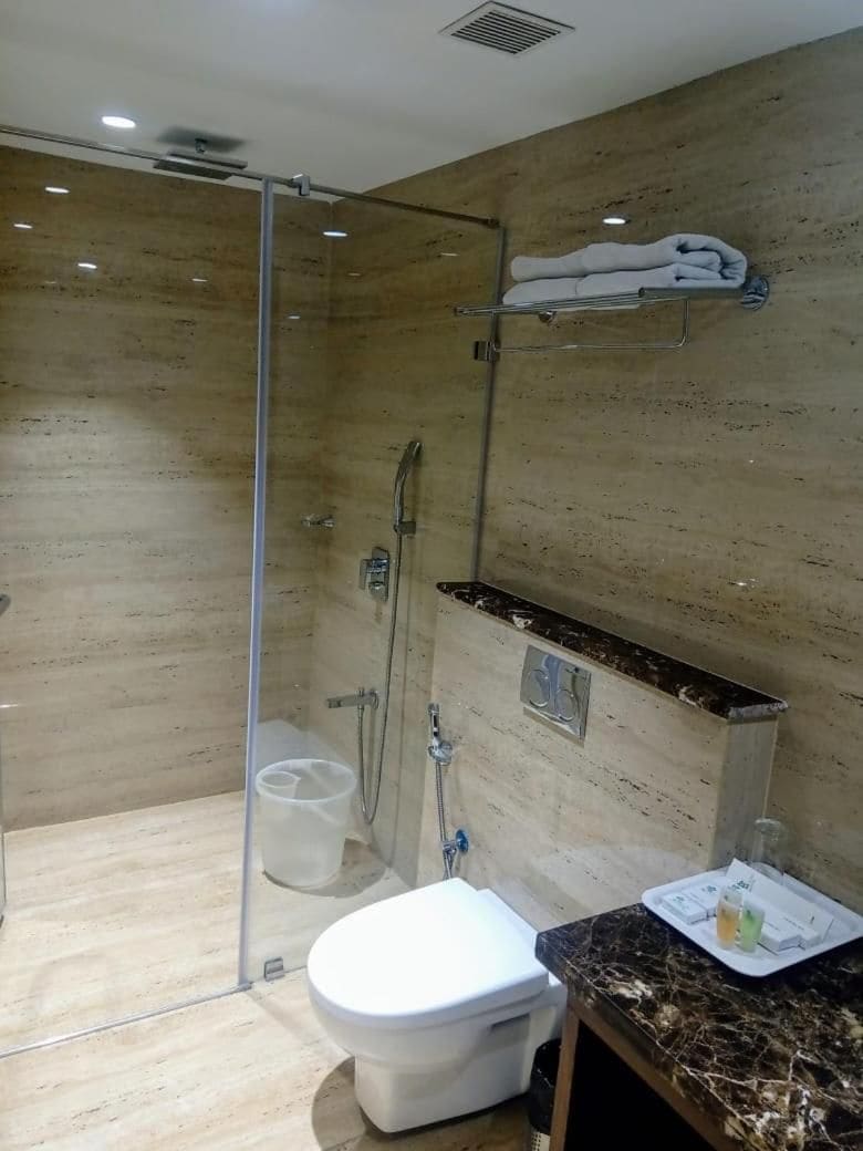 A bathroom with a glass-enclosed shower, a toilet, and a marble countertop with a towel rack.
