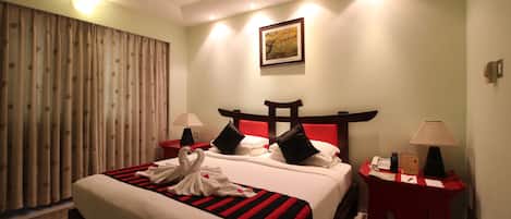 A hotel room with a large bed, two bedside tables, a red headboard, and a painting on the wall.