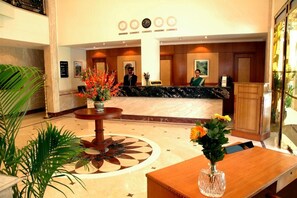 A hotel reception area with a marble counter, a receptionist, and a guest seated at the counter. - Beverly Hotel (Chennai)