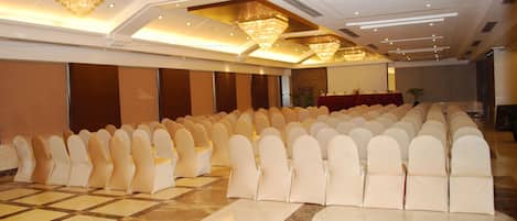 A banquet hall with rows of white chairs, a marble floor, and chandeliers.