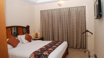 A hotel room with a bed, a nightstand, a lamp, a hanging coat rack, and a large window with curtains.