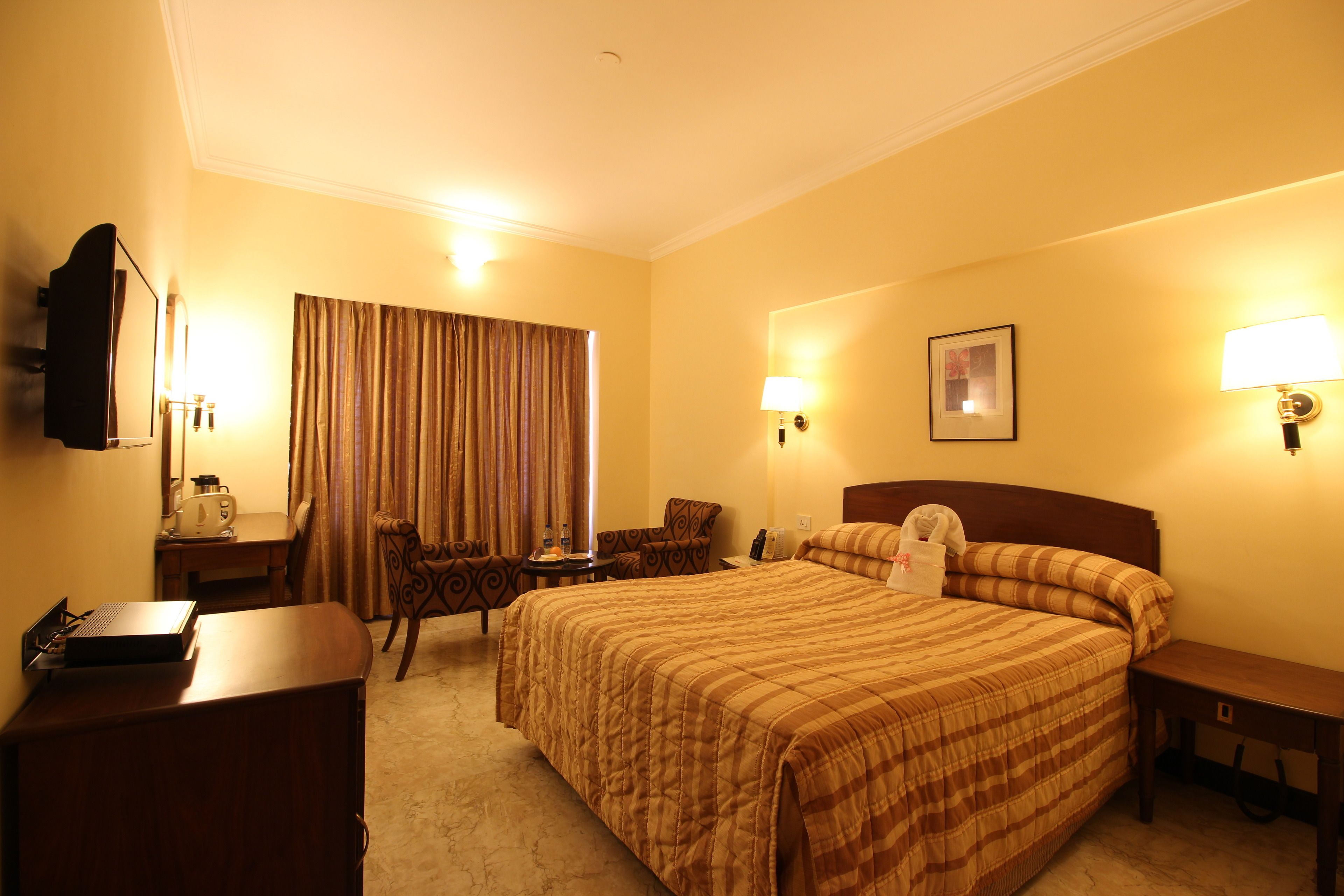 A hotel room with a large bed, a desk, a chair, a lamp, and a television.