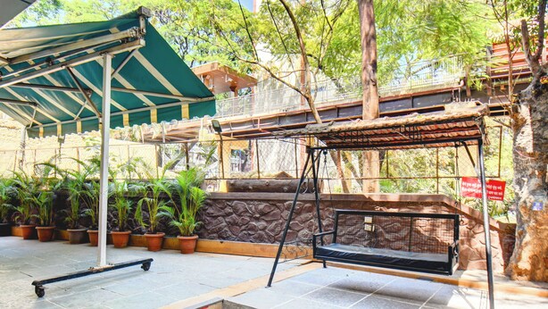A covered outdoor area with a swing, a skateboard, and potted plants. - MY BIZZ HOTEL (Pune)