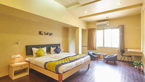 A hotel room with a bed, bedside table, chair, desk, and window. - MY BIZZ HOTEL (Pune)