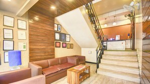 A hotel lobby with a brown leather sofa, a wooden coffee table, a staircase with a glass railing, and framed certificates on the wall. - MY BIZZ HOTEL (Pune)