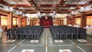 A conference room with rows of chairs facing a stage with a red backdrop. - Hotel Shreyas (Pune)