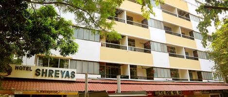 Un hotel de varios pisos llamado 'Hotel Shreyas', con techo de tejas rojas, balcones y una zona de recepción.