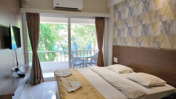 A hotel room with a bed, a TV mounted on the wall, an air conditioner, and a balcony with a table and chairs. - Hotel Shreyas (Pune)