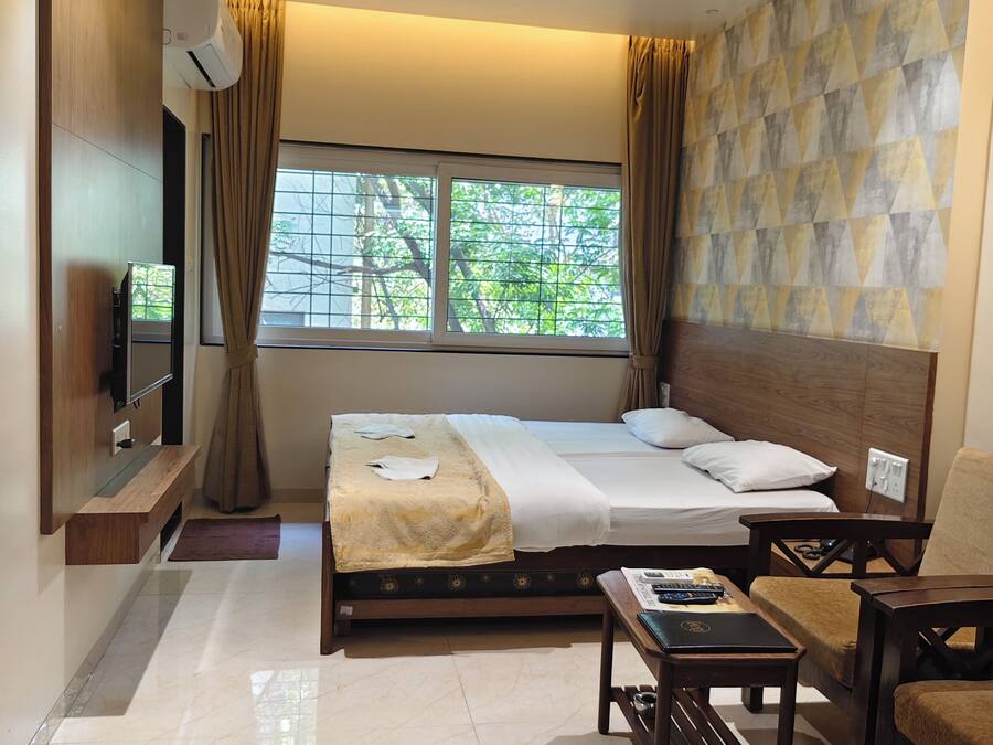 Quarto de hotel com cama, escrivaninha, cadeira, televisão e janela com cortinas.
