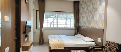 A hotel room with a bed, a sofa, a TV, a window with curtains, and a patterned wall.