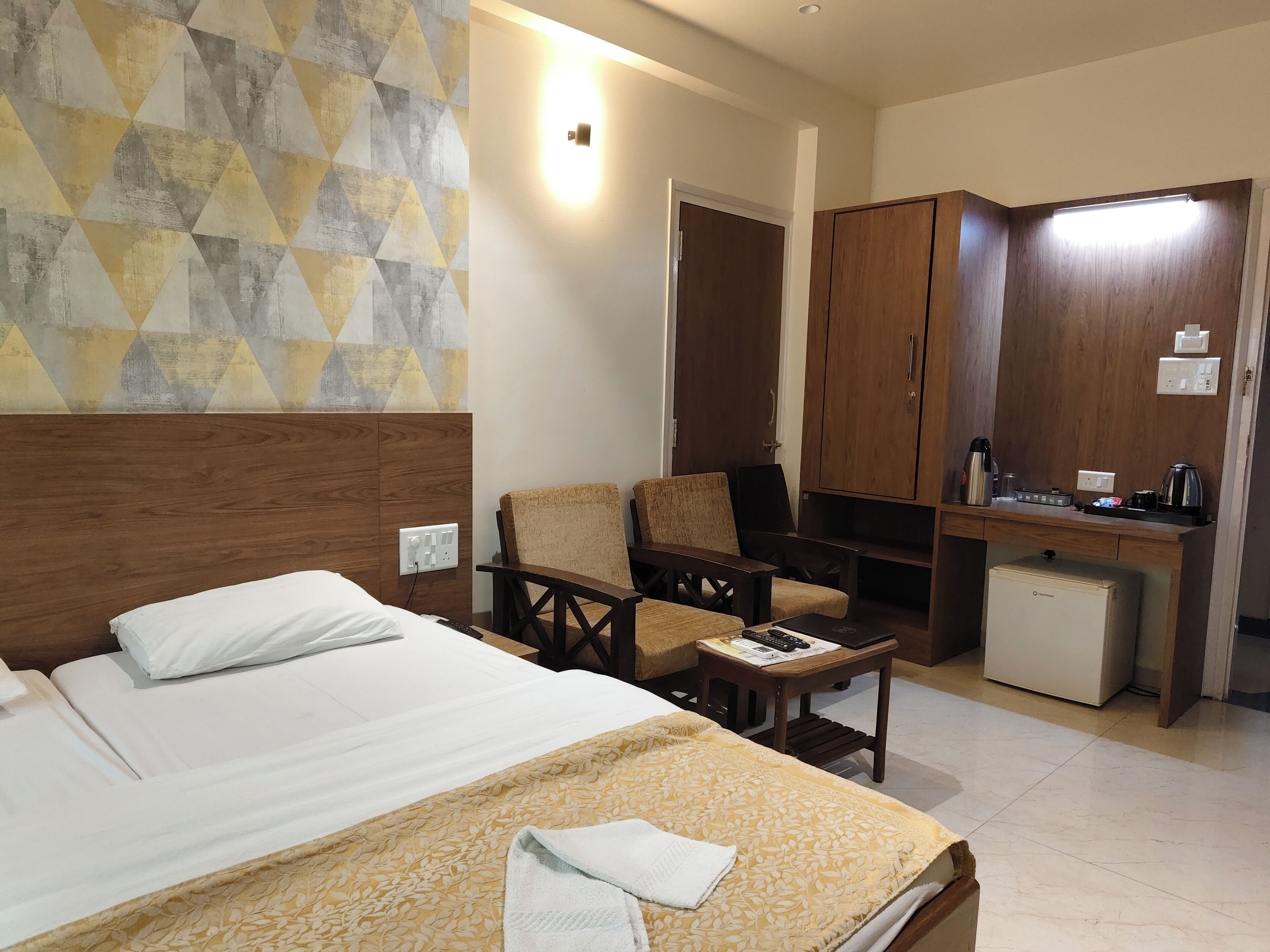 A hotel room with a bed, a desk, a chair, and a small refrigerator.