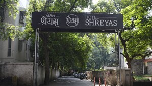 A hotel entrance with a sign in multiple languages, a paved driveway, and a motorcycle parked on the side. - Hotel Shreyas (Pune)