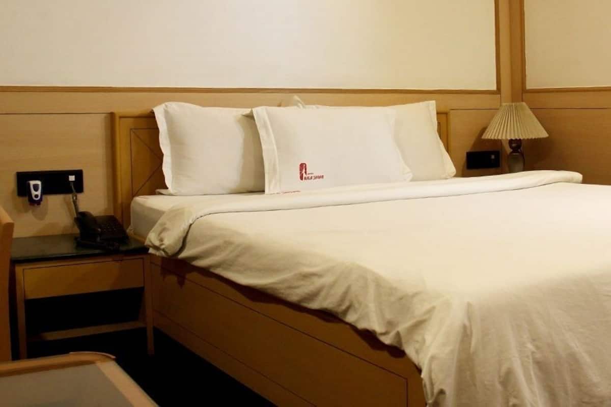 Una habitación de hotel con una cama, una mesita de noche con un teléfono, una lámpara y una silla.