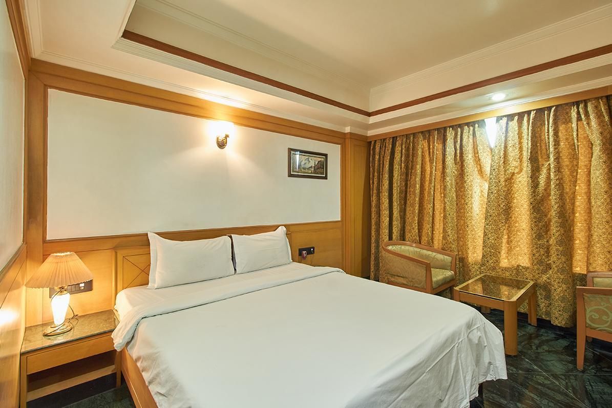 A hotel room with a large bed, a nightstand with a lamp, a chair, and a glass table.