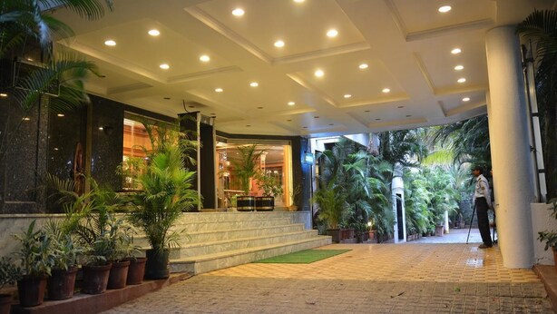 A hotel entrance with a covered walkway, potted plants, and a person standing by the entrance. - Hotel Kala Sagar (Pune)