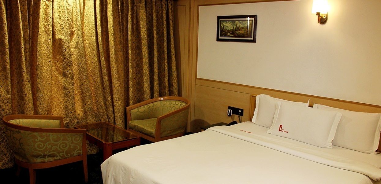 Habitación de hotel con cama, dos sillas, una mesita, un cuadro colgado en la pared y una mesita de noche.