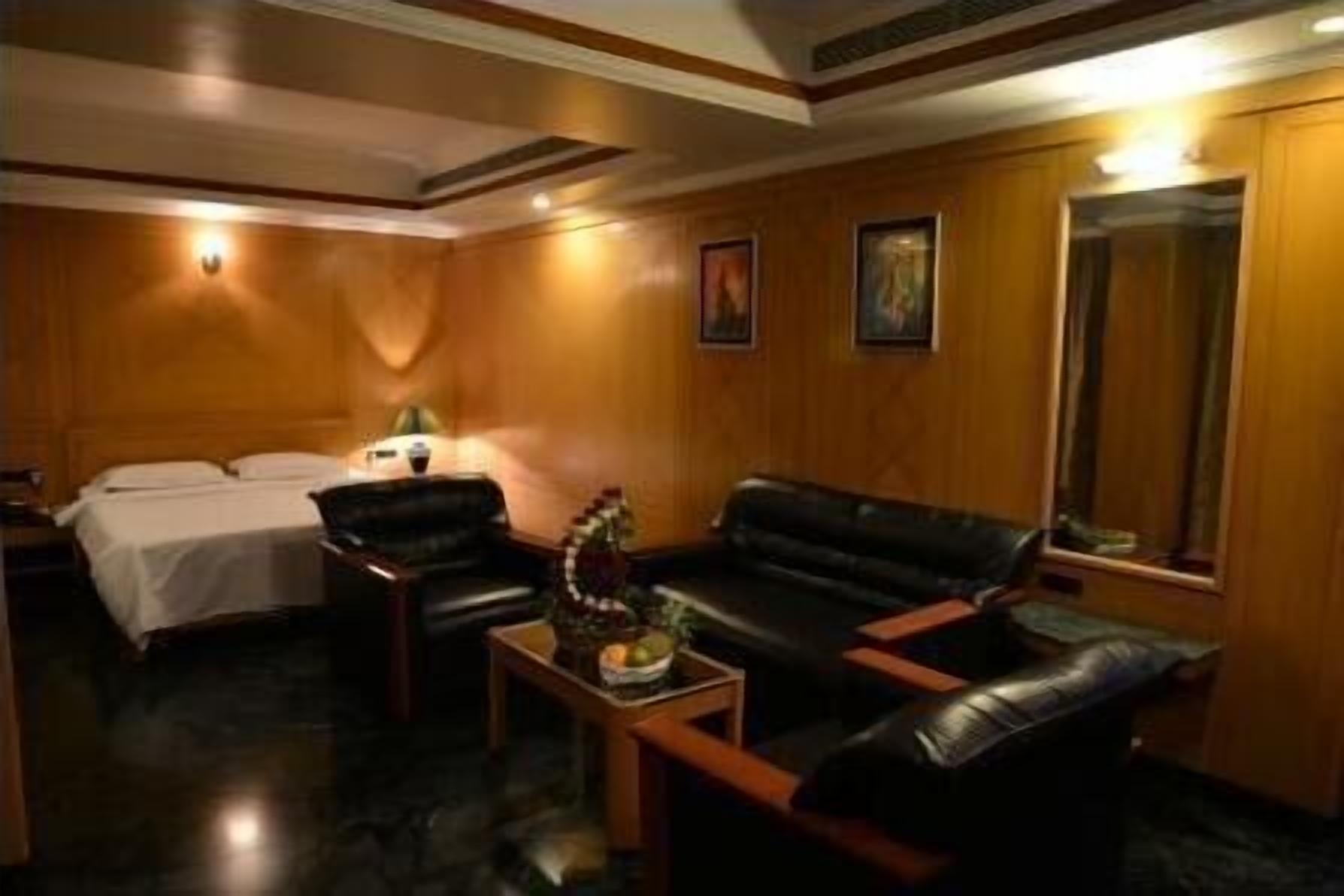 Une chambre d’hôtel avec un lit, un canapé en cuir noir, une petite table avec un vase et un grand miroir.