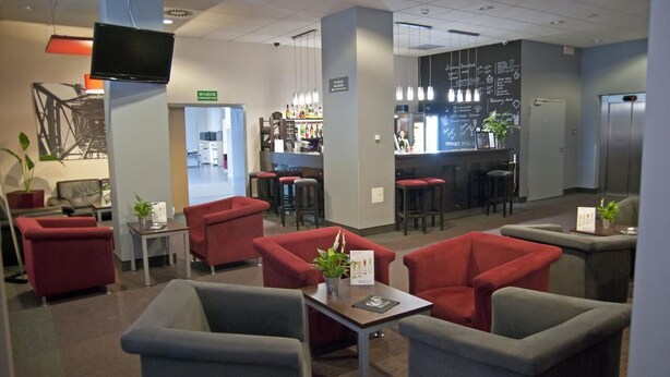 A modern lobby with red and grey seating, a bar area, and a television mounted on a pillar. - Quality Silesian Hotel (Katowice)