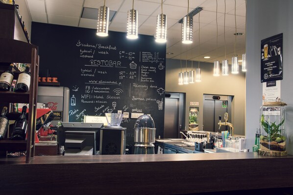 L’intérieur d’un café, avec un tableau noir servant de menu, des machines à expresso et une variété de grains de café exposés sur des étagères.