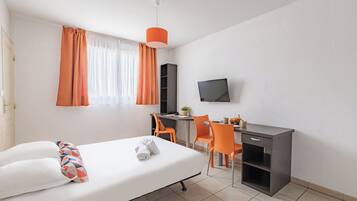 A hotel room with a bed, a desk, a chair, a TV, and a window with curtains.