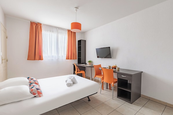 Habitación de hotel con cama, escritorio, silla, televisor y ventana con cortinas.