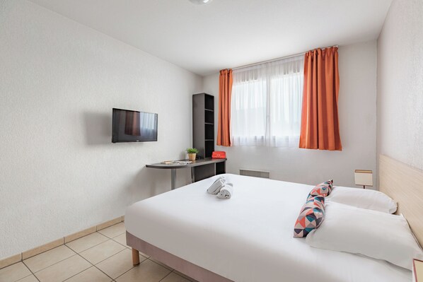A hotel room with a bed, a desk, a TV, and a window with curtains.