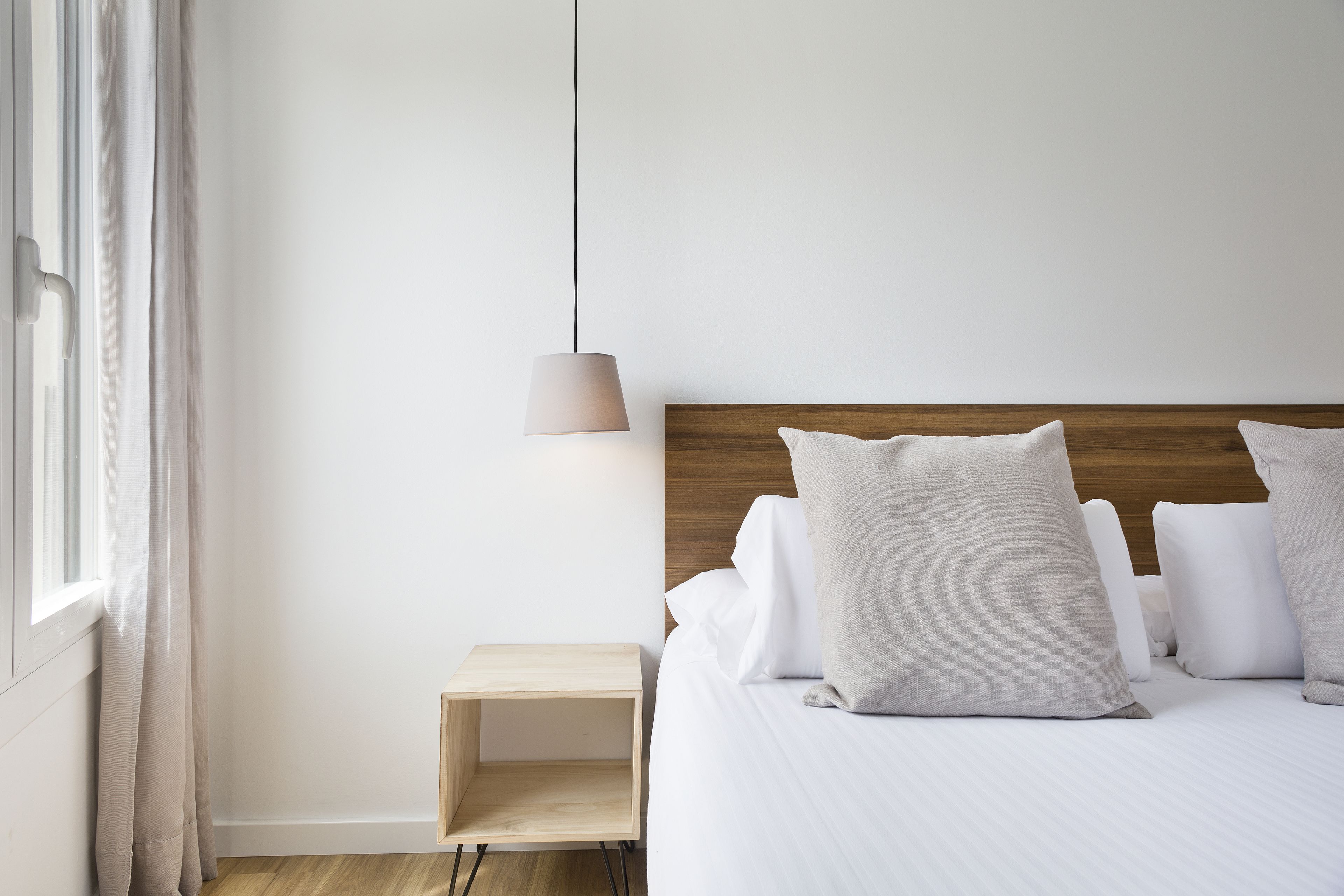 A neatly arranged bedroom with a wooden headboard, a bedside table, and a hanging lamp.