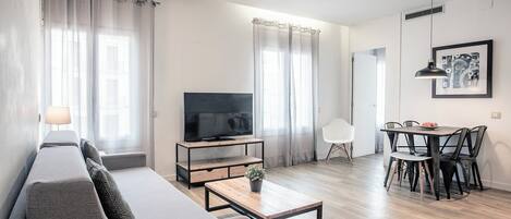 A modern living room with a sofa, TV, coffee table, and dining area.
