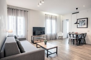 A modern living room with a sofa, TV, coffee table, and dining area. - Amister Apartments (Barcelona)
