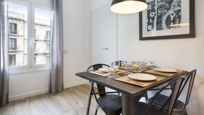 A dining area with a table set for four, a framed abstract artwork on the wall, and a window with curtains. - Amister Apartments (Barcelona)