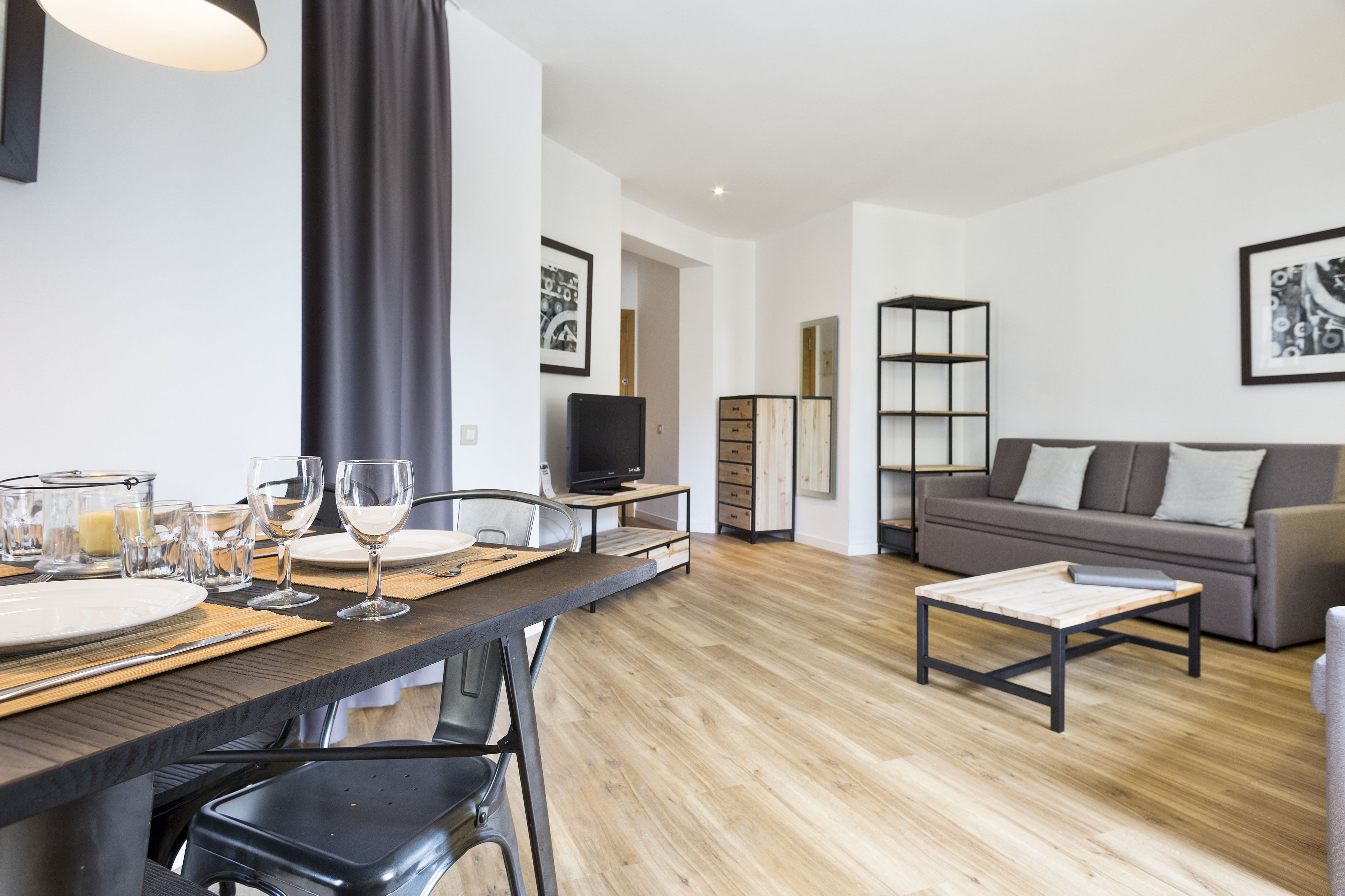 Una sala de estar moderna con comedor, un sofá gris, una mesa de centro y una televisión.