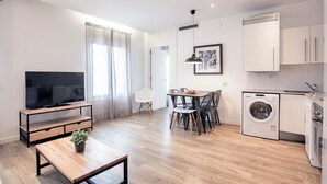 A modern kitchen with a washing machine, a dining area with chairs, a TV on a stand, and a potted plant. - Amister Apartments (Barcelona)
