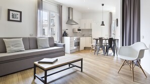 A modern living room with a grey sofa, a wooden coffee table, and a dining area with a white chair and a table. - Amister Apartments (Barcelona)