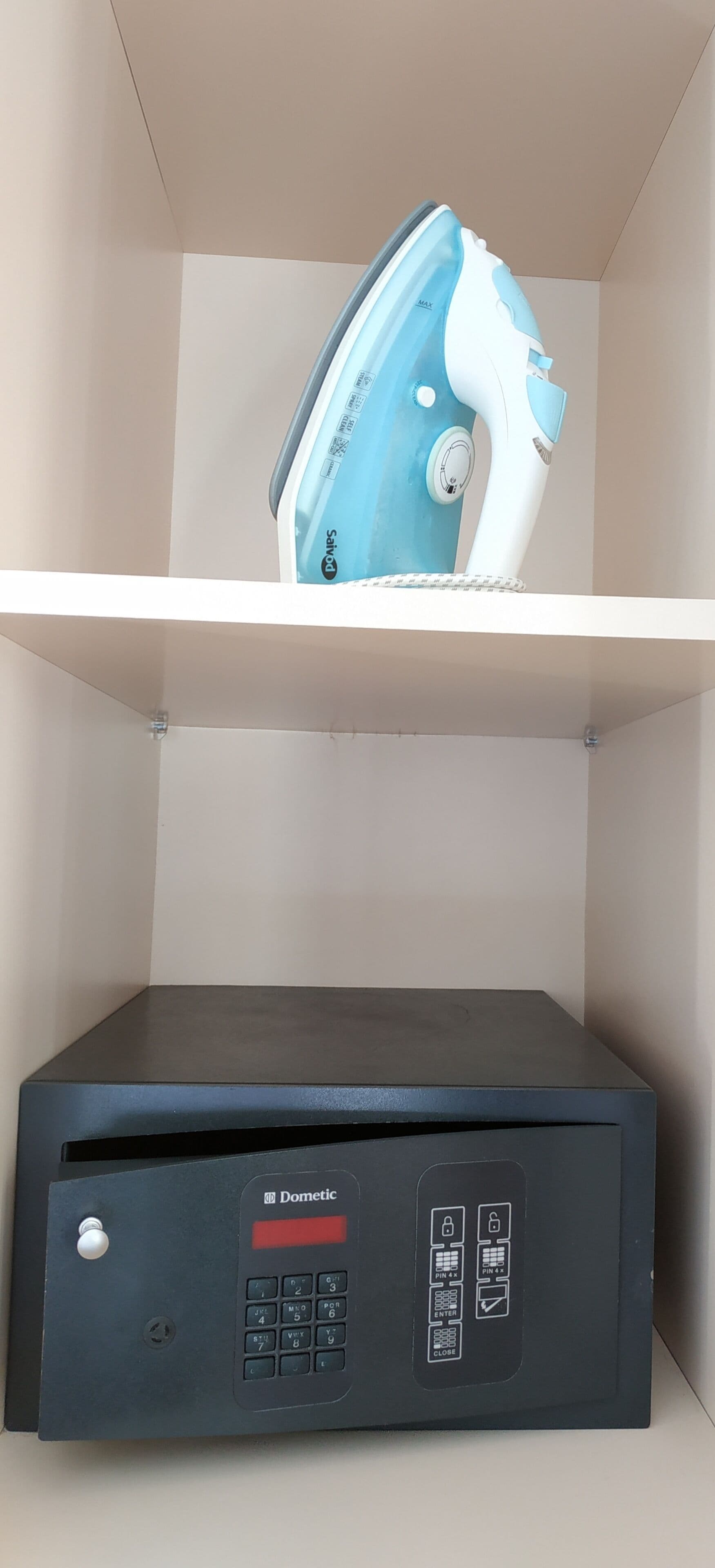 A room with a blue and white iron on a shelf and a black security device labeled "Dometic" below it.