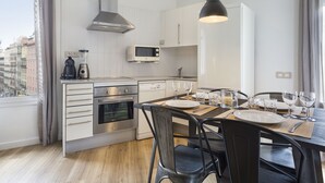 A modern kitchen with stainless steel appliances, a dining area with a table set for two, and a view of the city through large windows. - Amister Apartments (Barcelona)