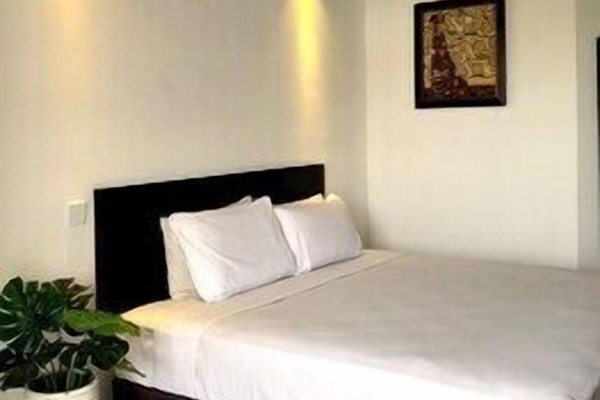 Une chambre à coucher comprenant un lit, un luminaire fixé au mur, une œuvre d’art encadrée et une plante en pot.