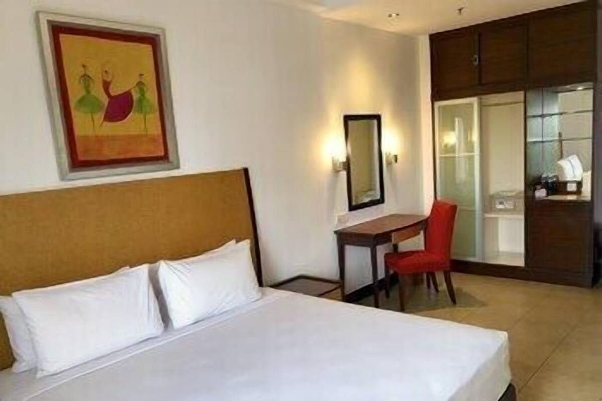 Une chambre d’hôtel avec un lit, un bureau, une chaise, un miroir et un tableau au mur.