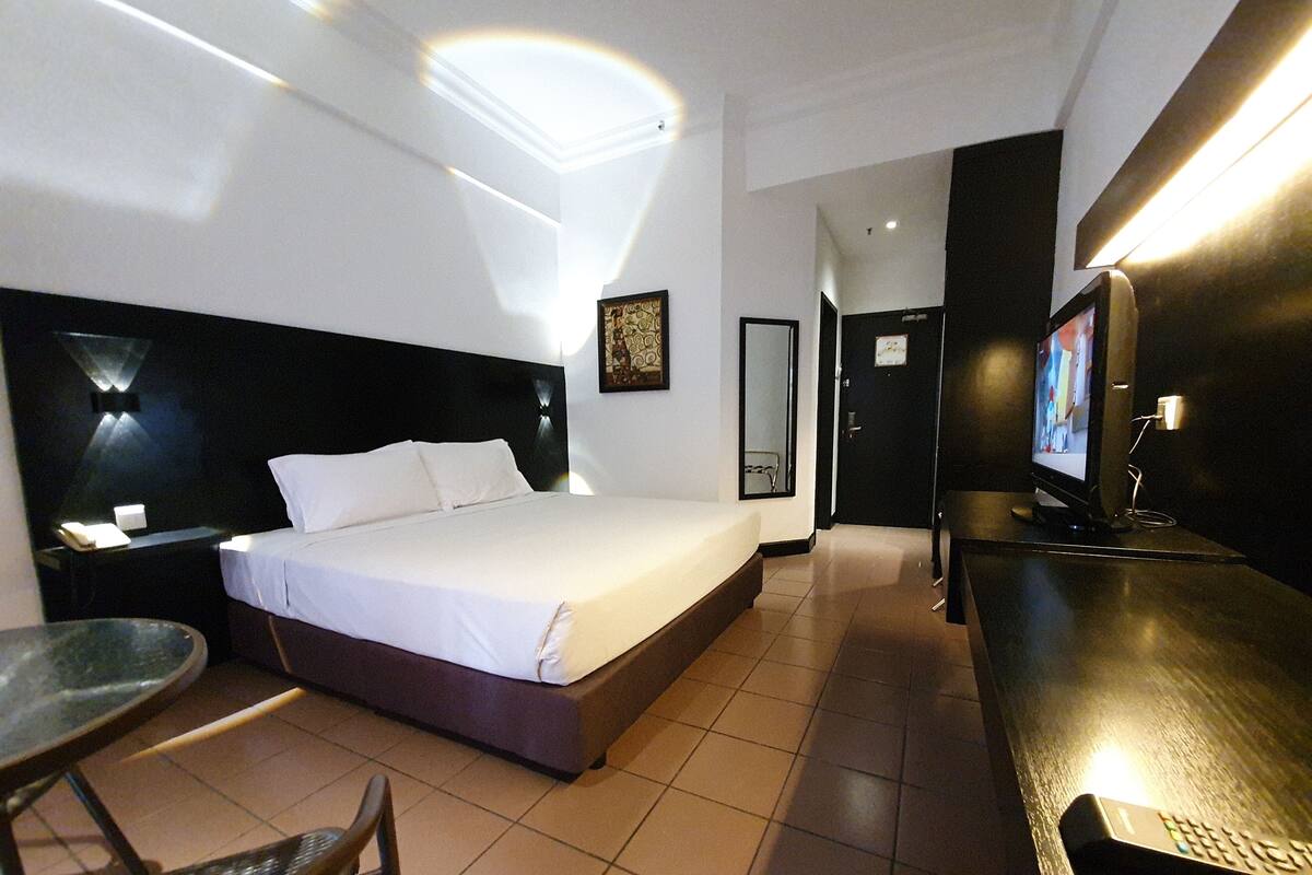 Une chambre d’hôtel comprenant un lit, une table de chevet, une chaise, une télévision et une petite table.